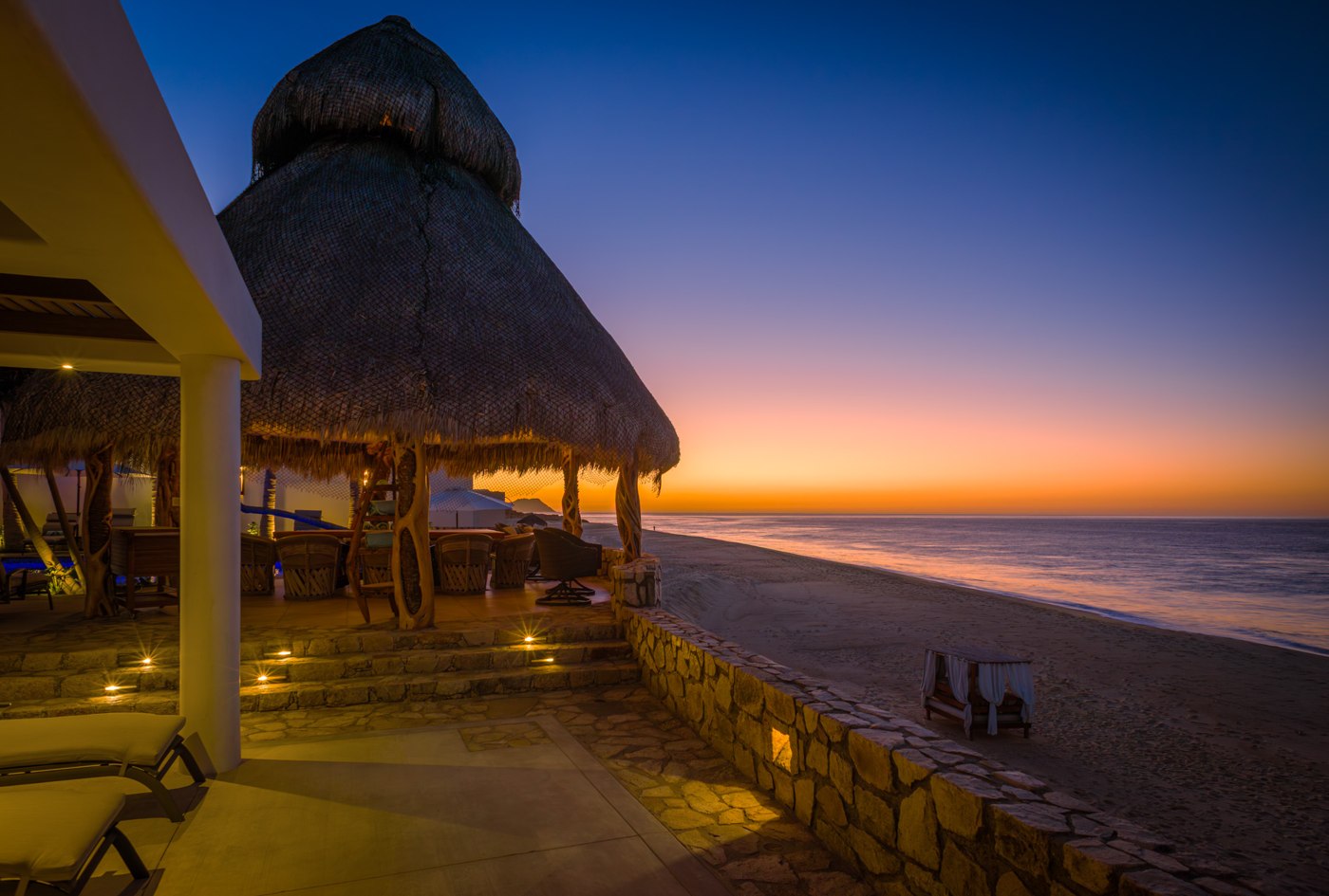 A warmly lit coastal terrace and palapa beside a quiet beach