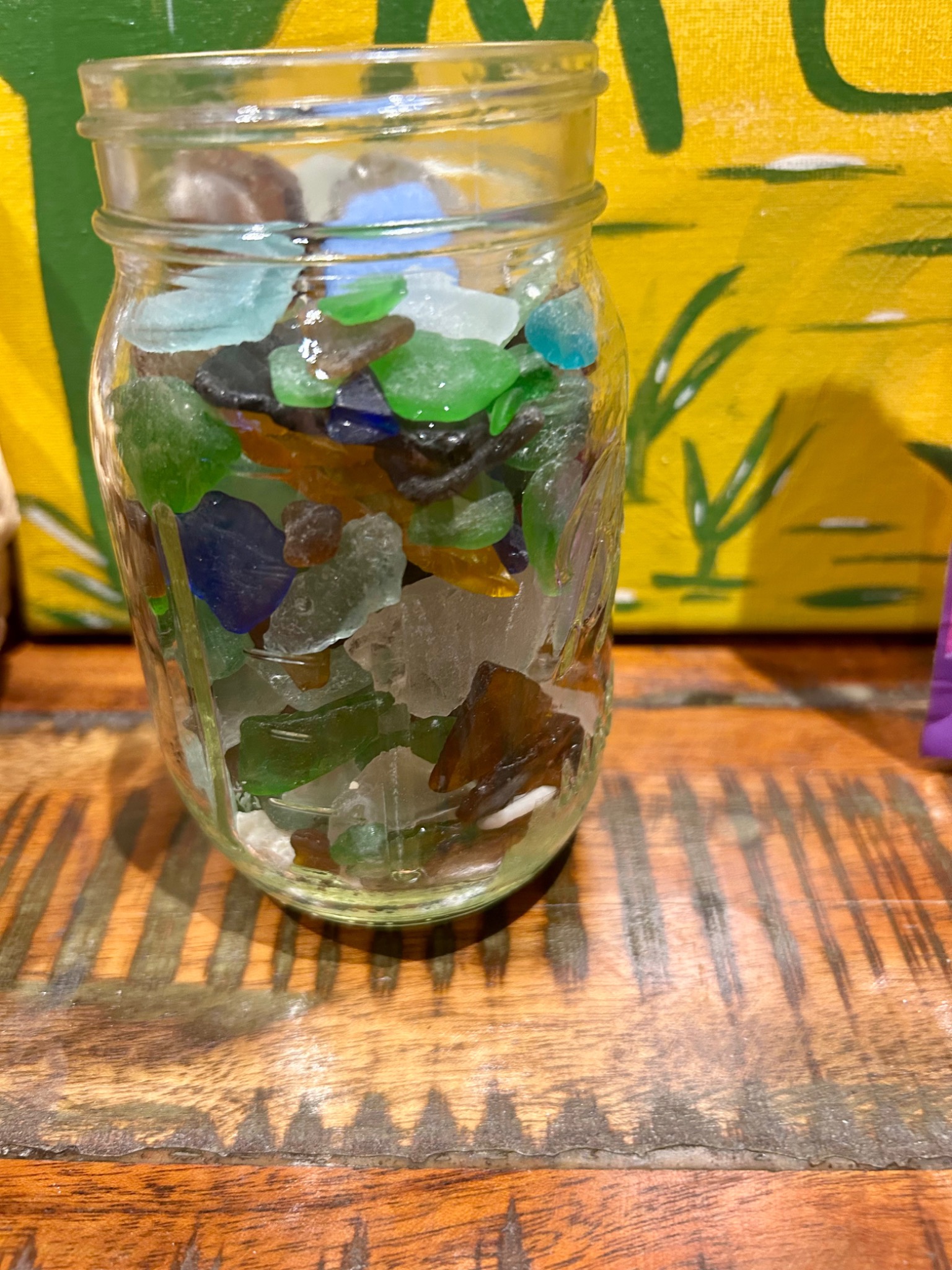 A clear jar filled with green, blue, amber and frosted white sea glass